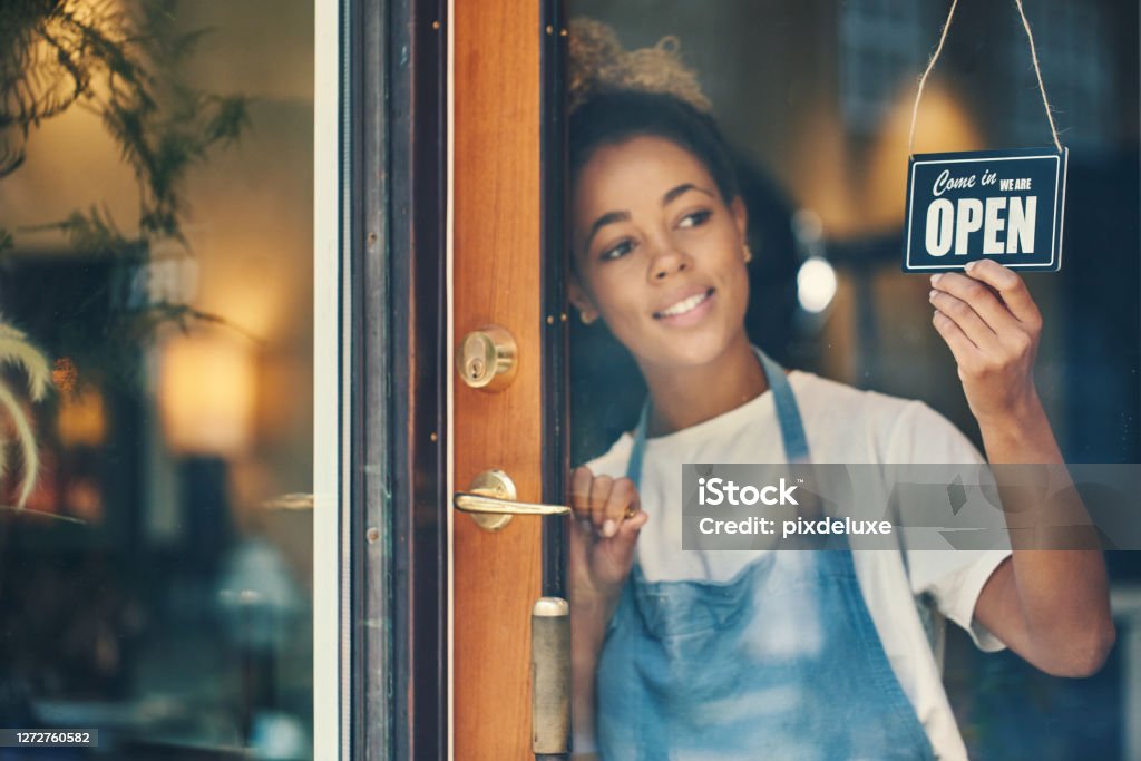 Plan d'une jeune femme accrochant un panneau 'Ouvert' à la fenêtre d'un café