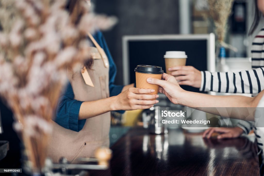 Le barista a servi une tasse de café chaud à emporter au client au comptoir du café-restaurant, concept de propriétaire de café, esprit de service de la serveuse